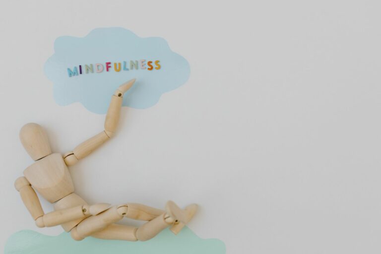 Wooden mannequin with mindfulness text on light blue cloud background, conveying calm.