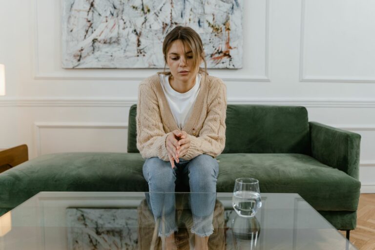 Woman sitting on a green sofa with a pensive expression, reflecting indoors.